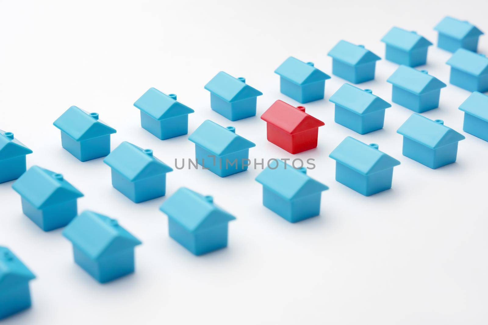 Real estate and property market in cottage village. Mortgage and buying a house. Red miniature house model among blue toy houses arranged in three rows different from group of same type miniature home by synel