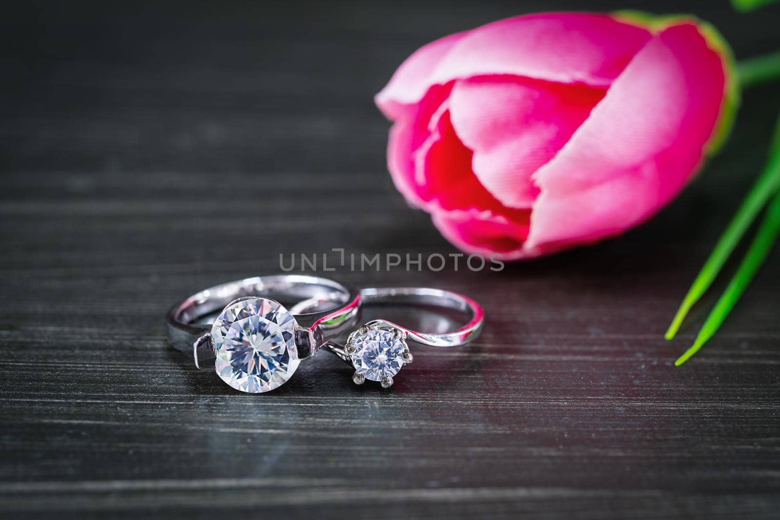 Close up Diamond gem wedding rings with pink tulip flower on black background