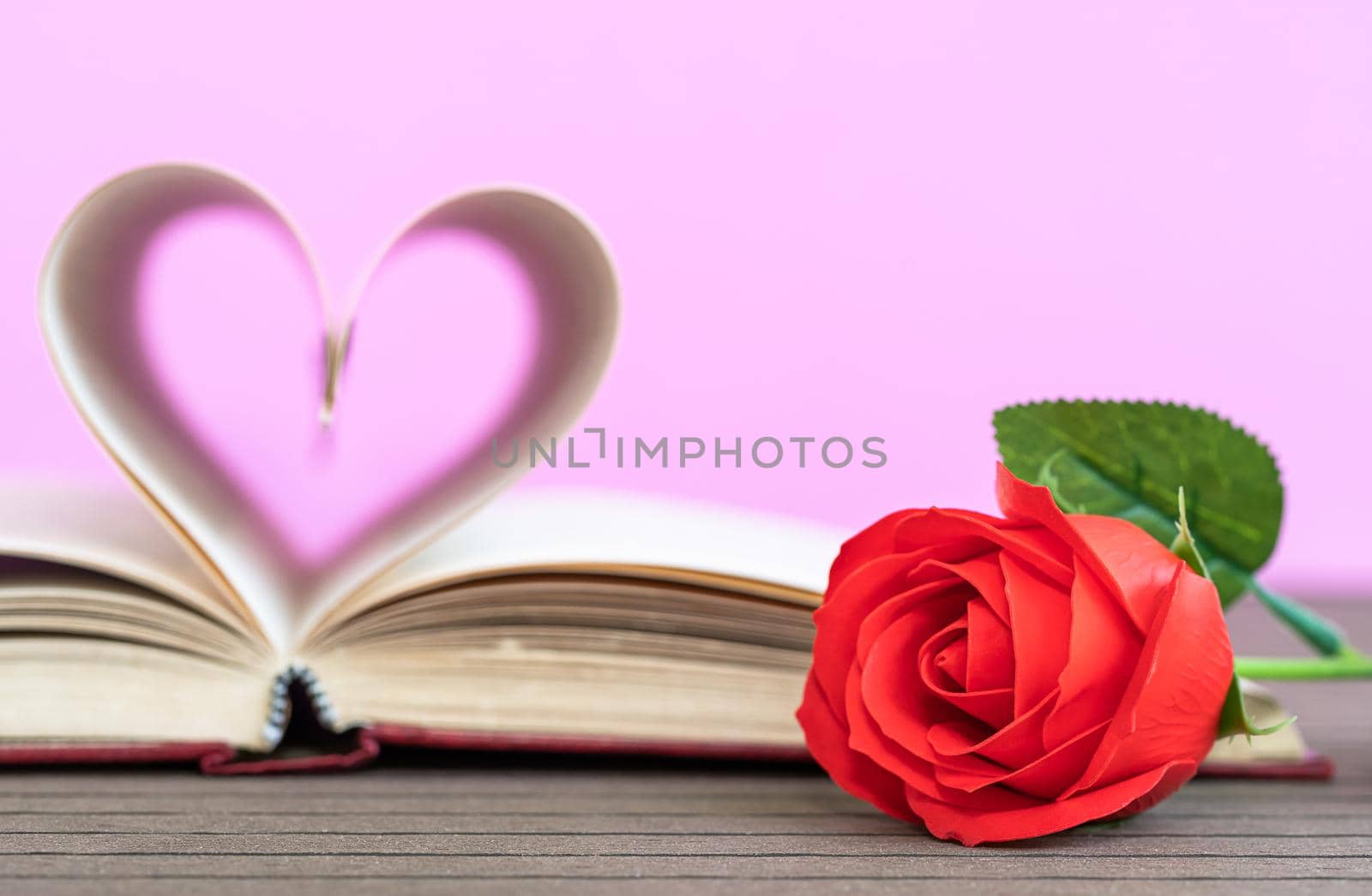 Pages of book curved into a heart shape and red rose. Love concept of heart shape from book pages on pink background