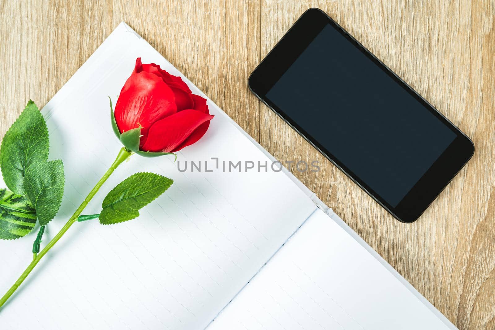 Top view shot of red roses on blank notebook diary and  smartphone on wood table,Valentine concept