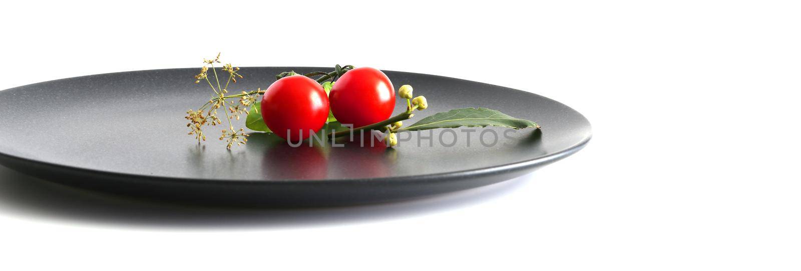Table arrangement with tomato on black plate on white background. Food preparation, presentation