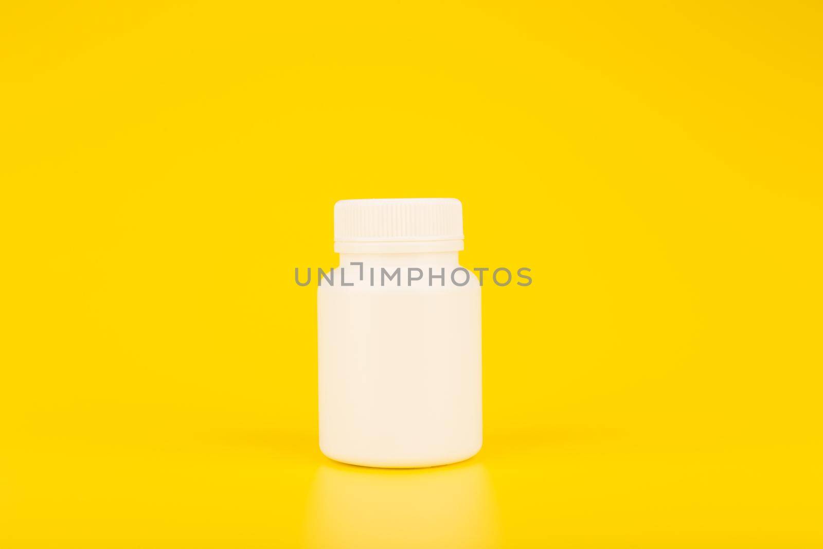 Minimalistic still life white plastic medication bottle against yellow background with copy space. Simple and creative concept of pharmacy, medical treatment or vitamins for kids. 