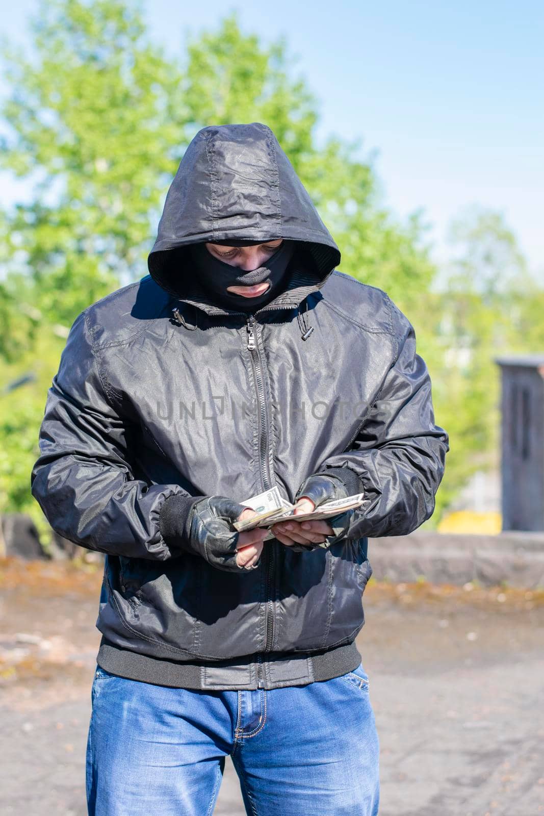 a bandit in a black mask stands on the street and counts the stolen money by jk3030