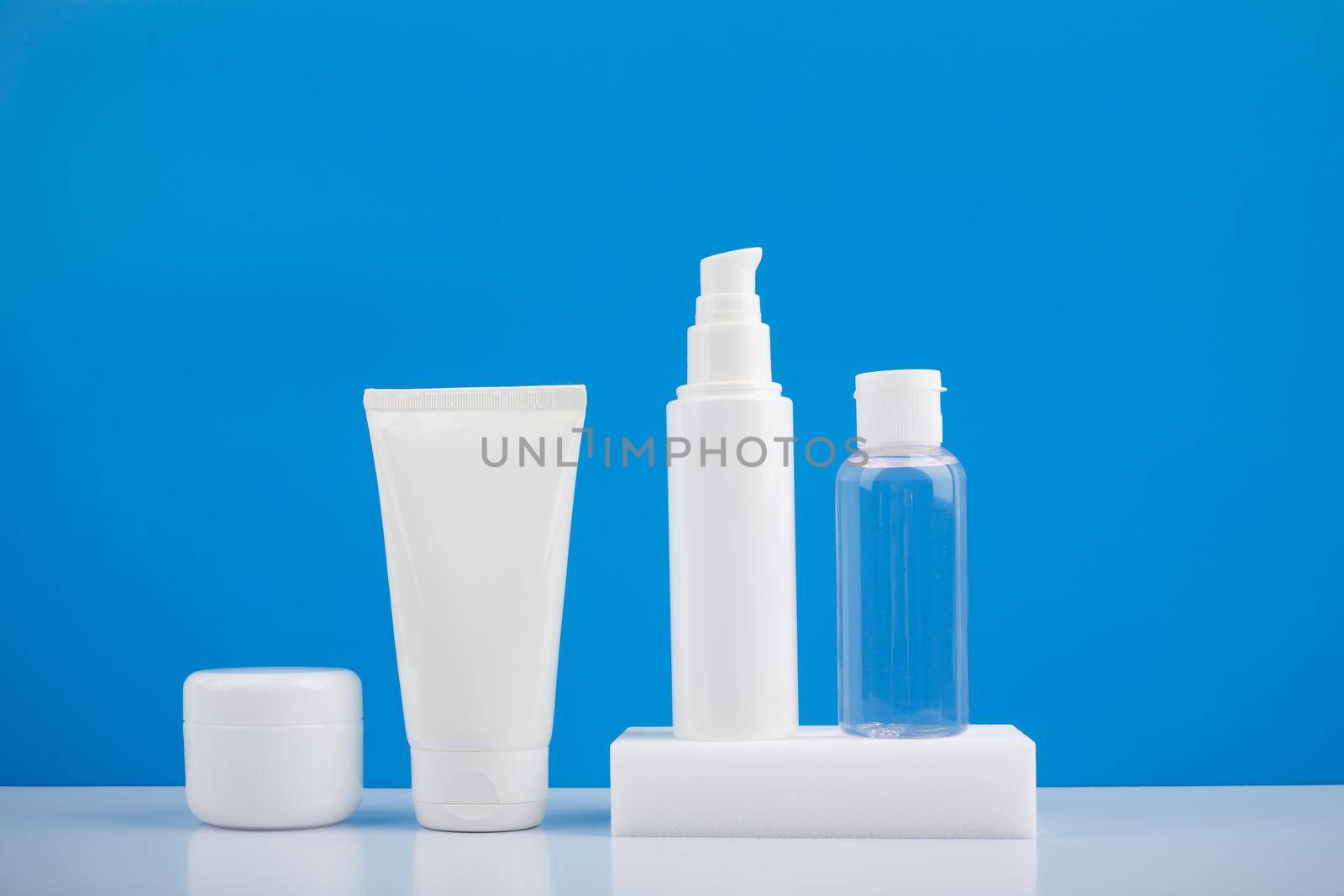 Minimalistic still life with set of cosmetic products for daily skincare on white table against blue background. High quality photo