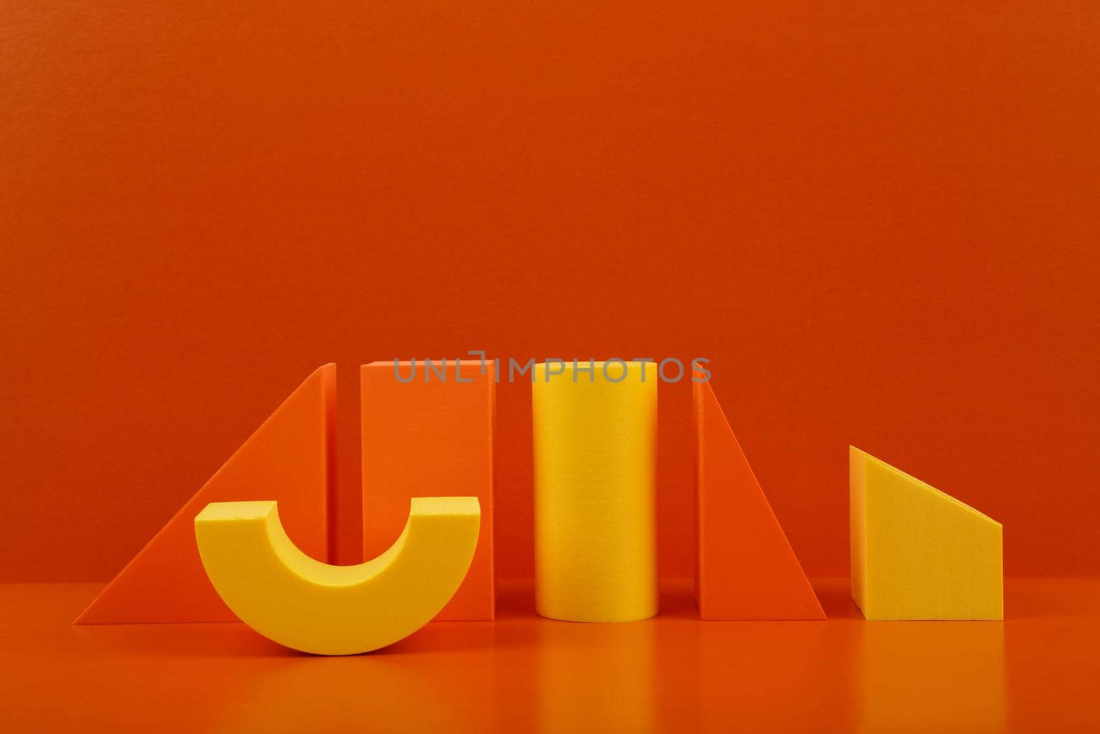 Abstract duotone geometric composition with orange and yellow figures on orange reflective table against orange background with copy space. 