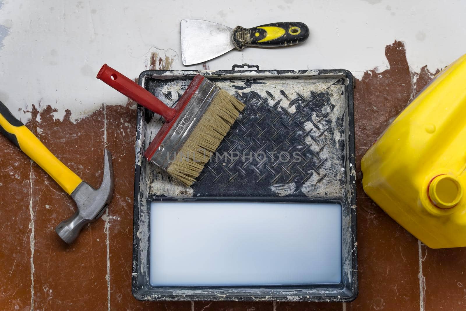 A hammer,a spatula,a paint brush,a canister and a tray for paints lie on the floor during the repair and restoration of the house.Work as a Builder or handyman in the house.Repairing a room by YevgeniySam