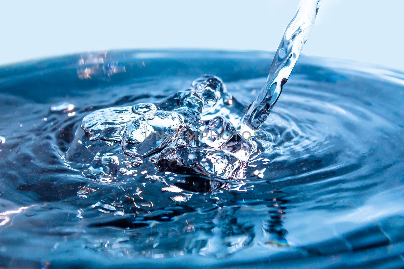 A flowing stream of blue water. Splash of water close-up. Frozen water drop photographed at high speed.Slow dripping of liquid with air bubbles. Nature backgrounds or Wallpaper.Frozen liquid splashes by YevgeniySam