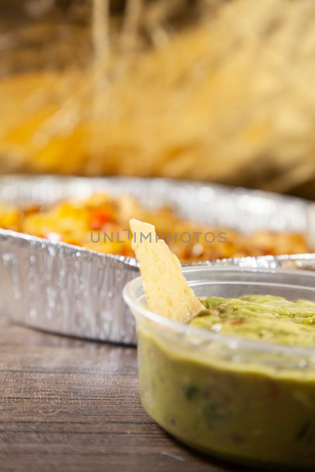 Tortilla chip in a container of guacamole with a tin of food in the background, in a dark, golden fall colors