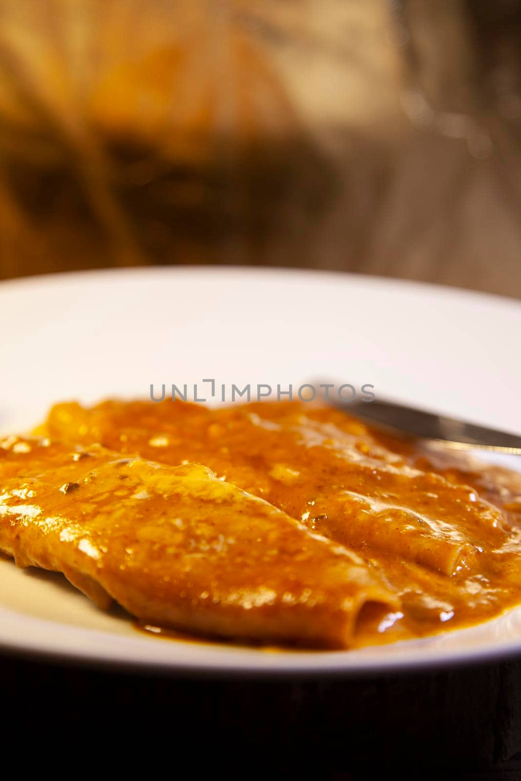 Close up of two cheesy enchiladas on a white plate