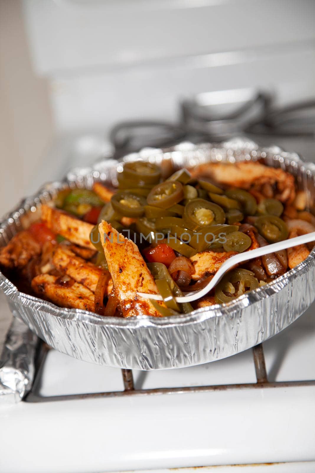 Stir fried chicken in a serving tin with jalapenos, roasted green bell peppers, roasted onions, and roasted red peppers