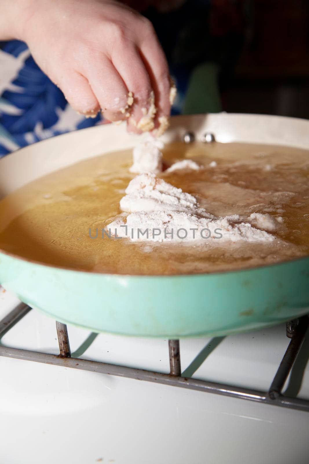 Woman dropping breaded chicken into a frying pan with hot grease