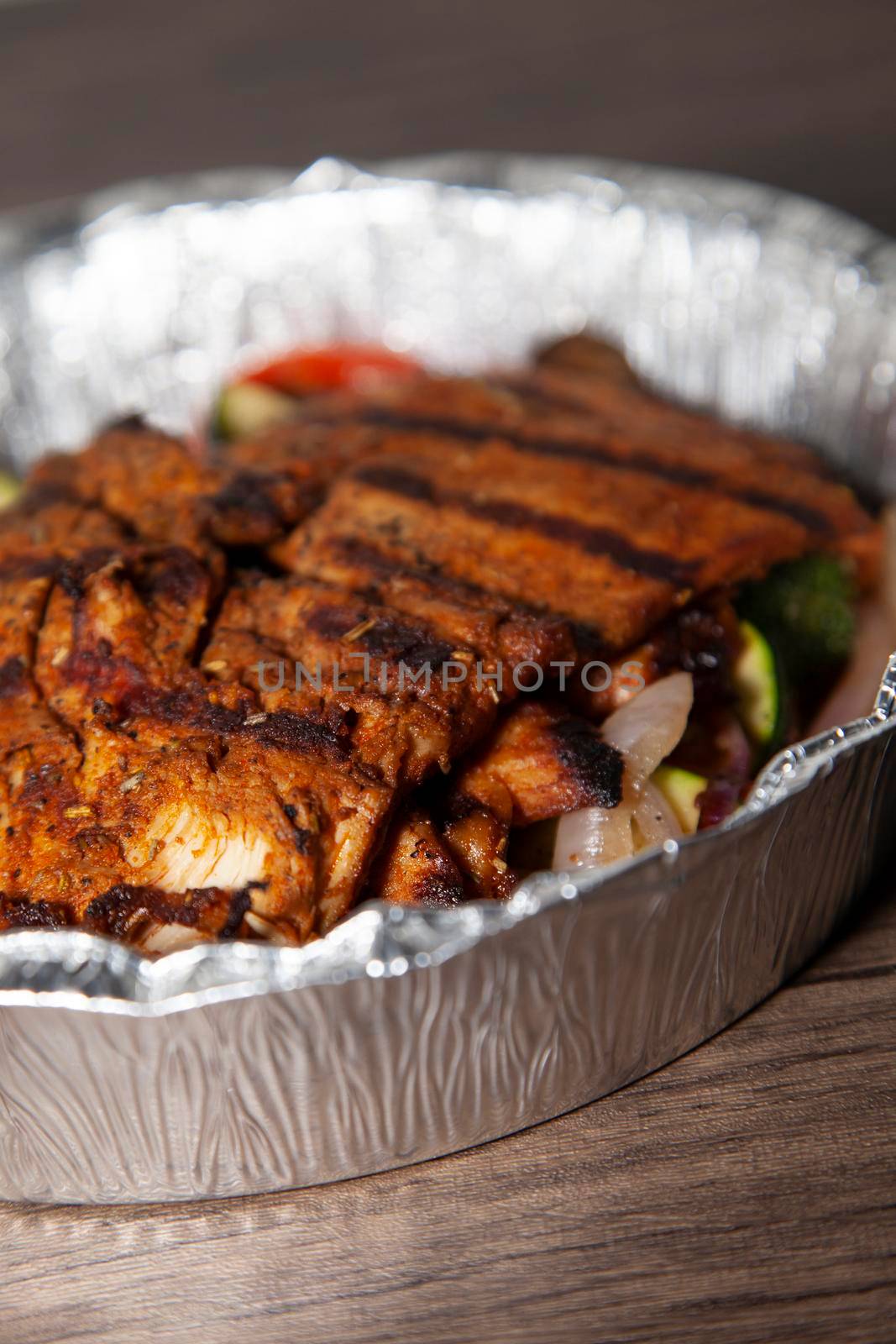 Grilled chicken breast, tomato and grilled broccoli, mushrooms, and zucchini in a takeout container