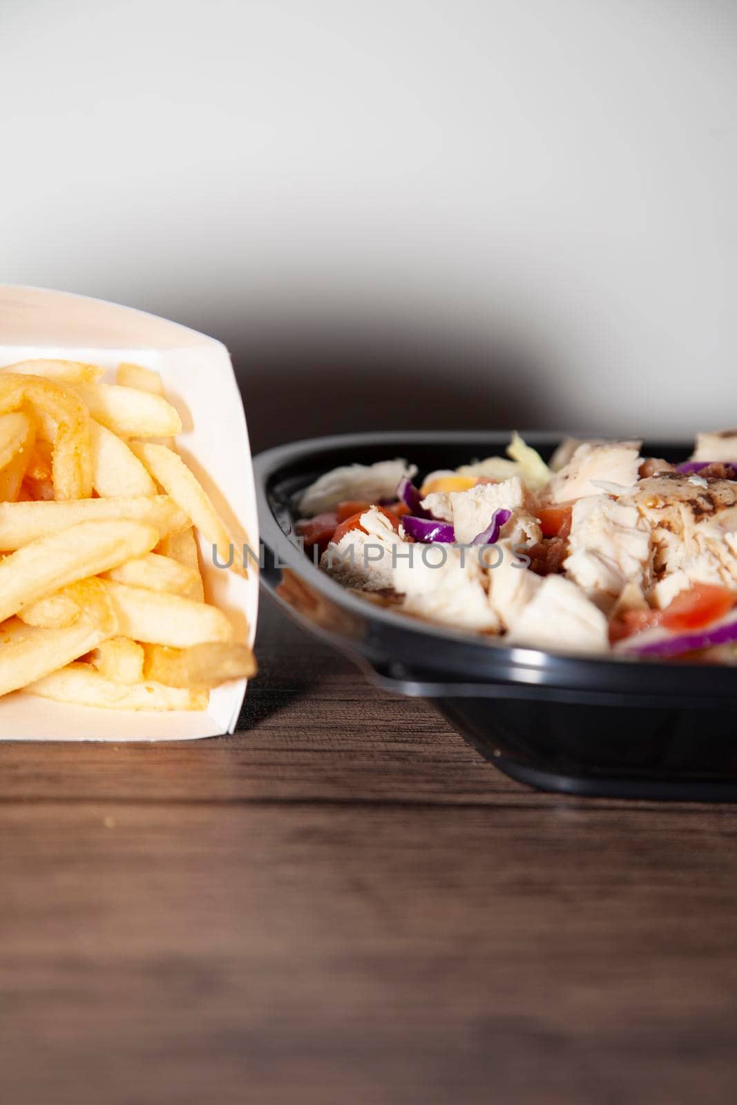 French fries next to grilled chicken, bacon, lettuce, cabbage, shredded cheese, and diced tomato salad in a takeout container