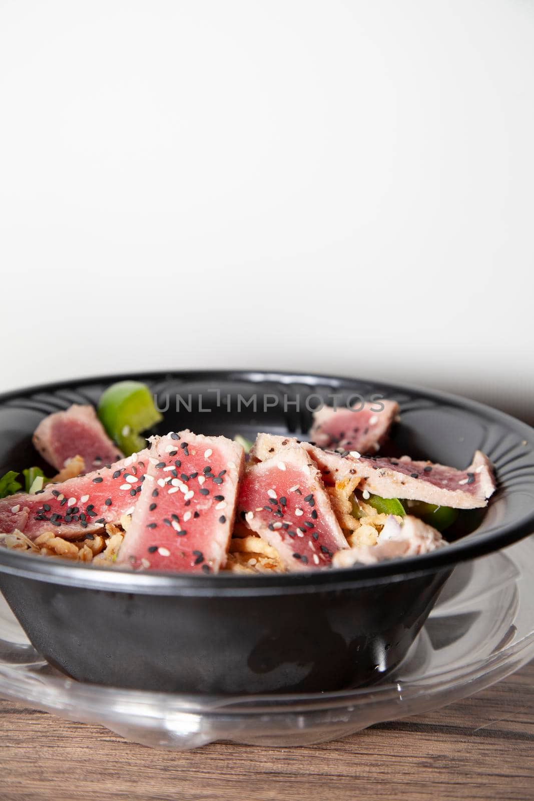 Seared tuna salad with lettuce, sliced green bell pepper, and red onion on a wooden table 