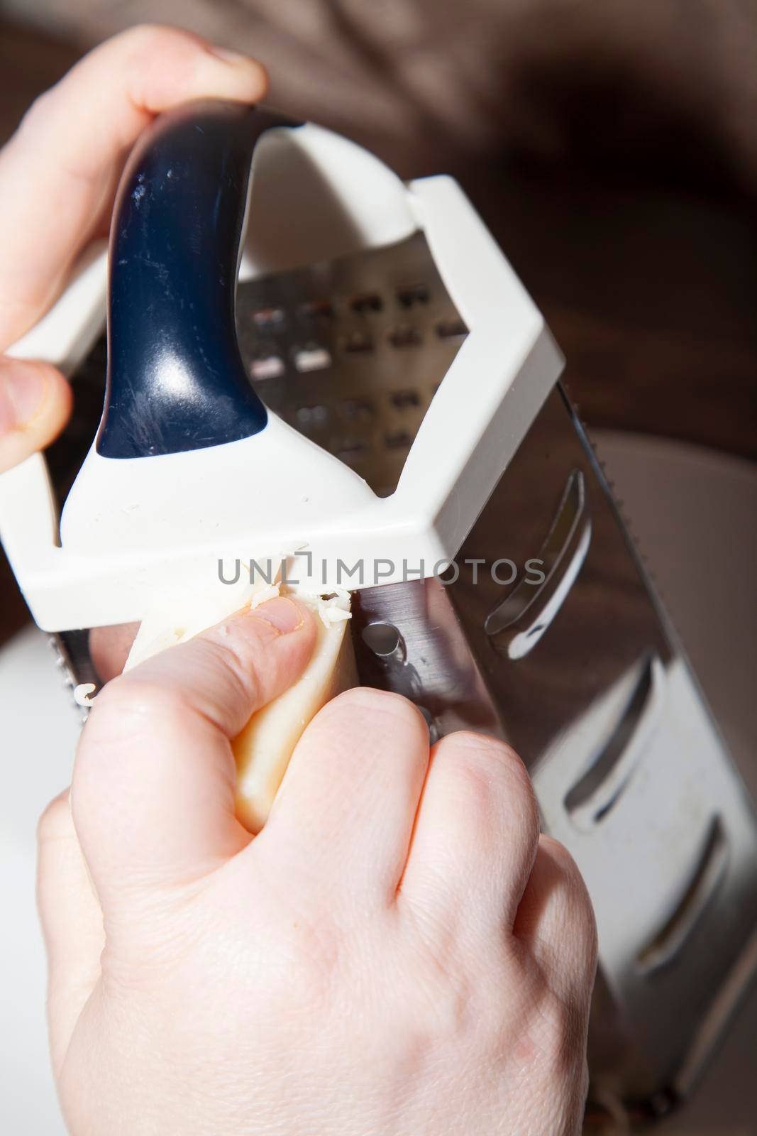 Woman using a large, metal cheese grater to shred white cheese on a white plate