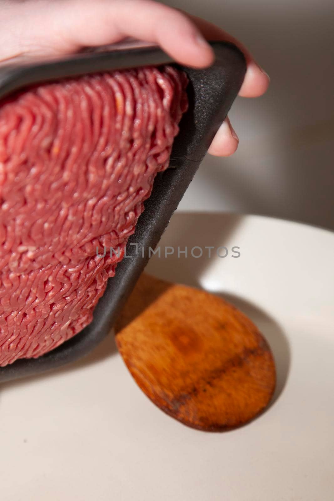 Woman dumping an open package of angus ground beef into a frying pan