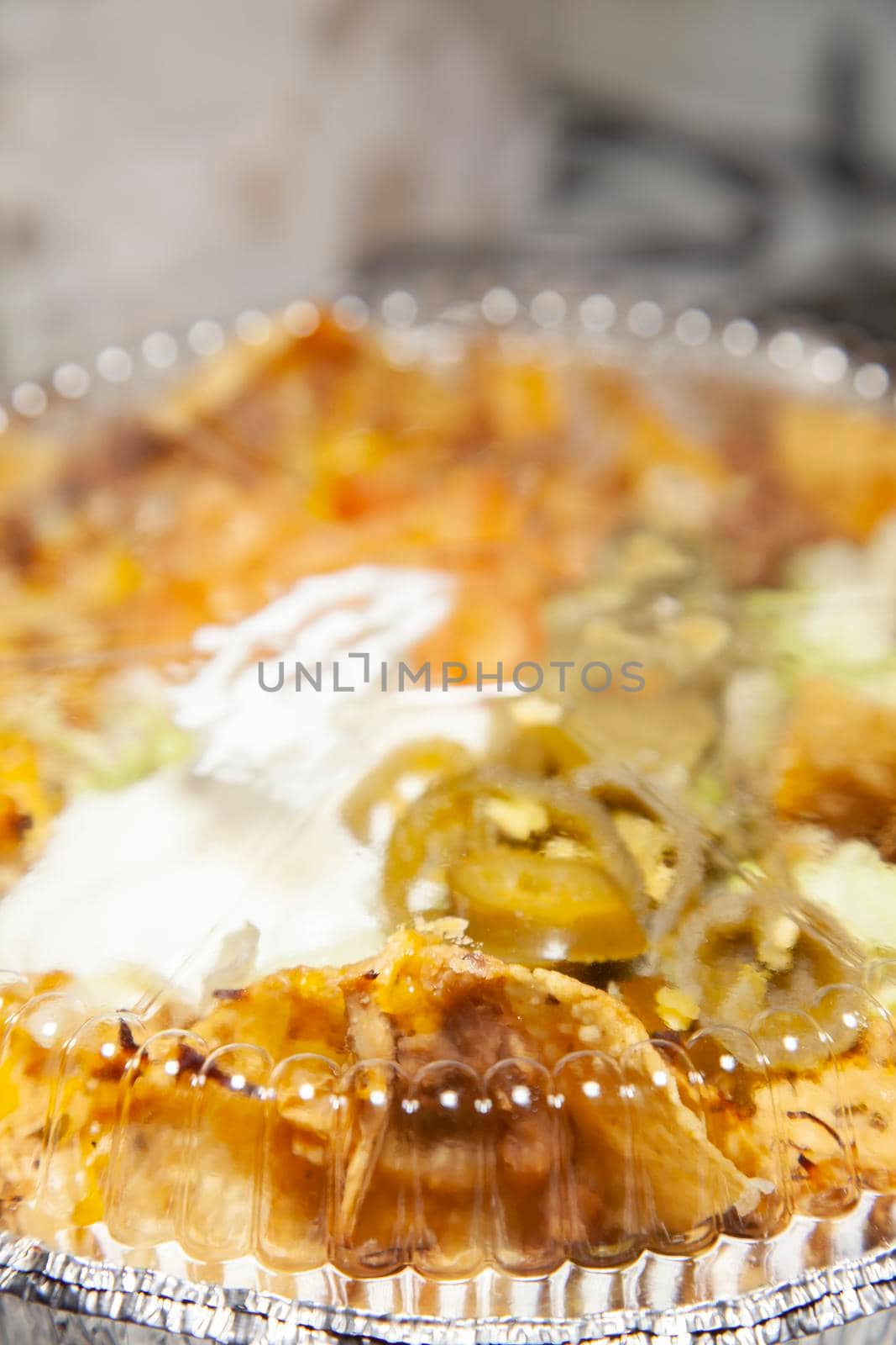 Takeout tin of nachos with sour cream, chips, jalapenos, guacamole, and cheese