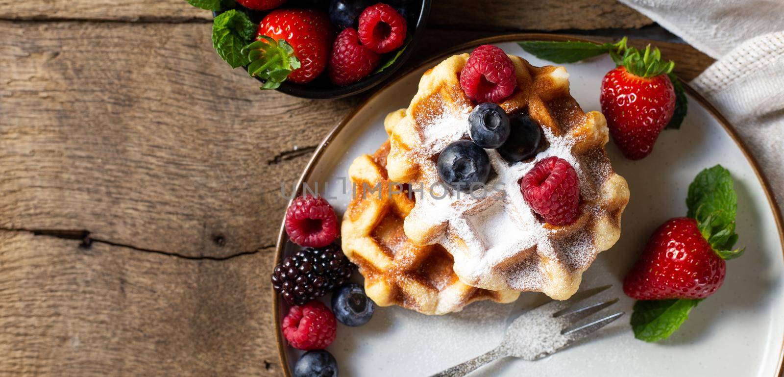 home made sweets with berries. Top view. Belgian waffles strawberries, blueberries on plate with canvas on old wood background. Breakfast on rustic kitchen