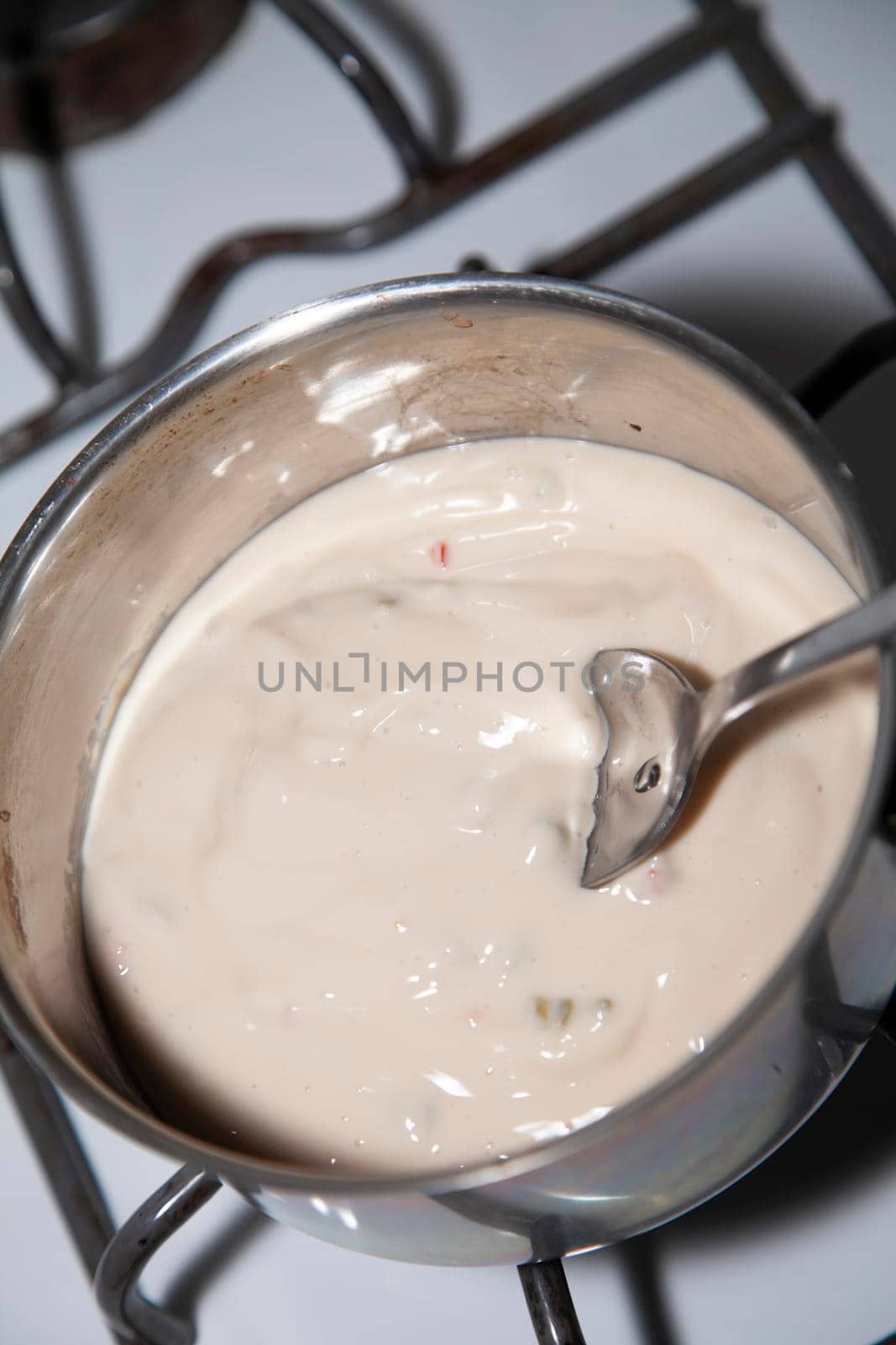 White queso cheese boiling in a pot with a silver spoon for stirring
