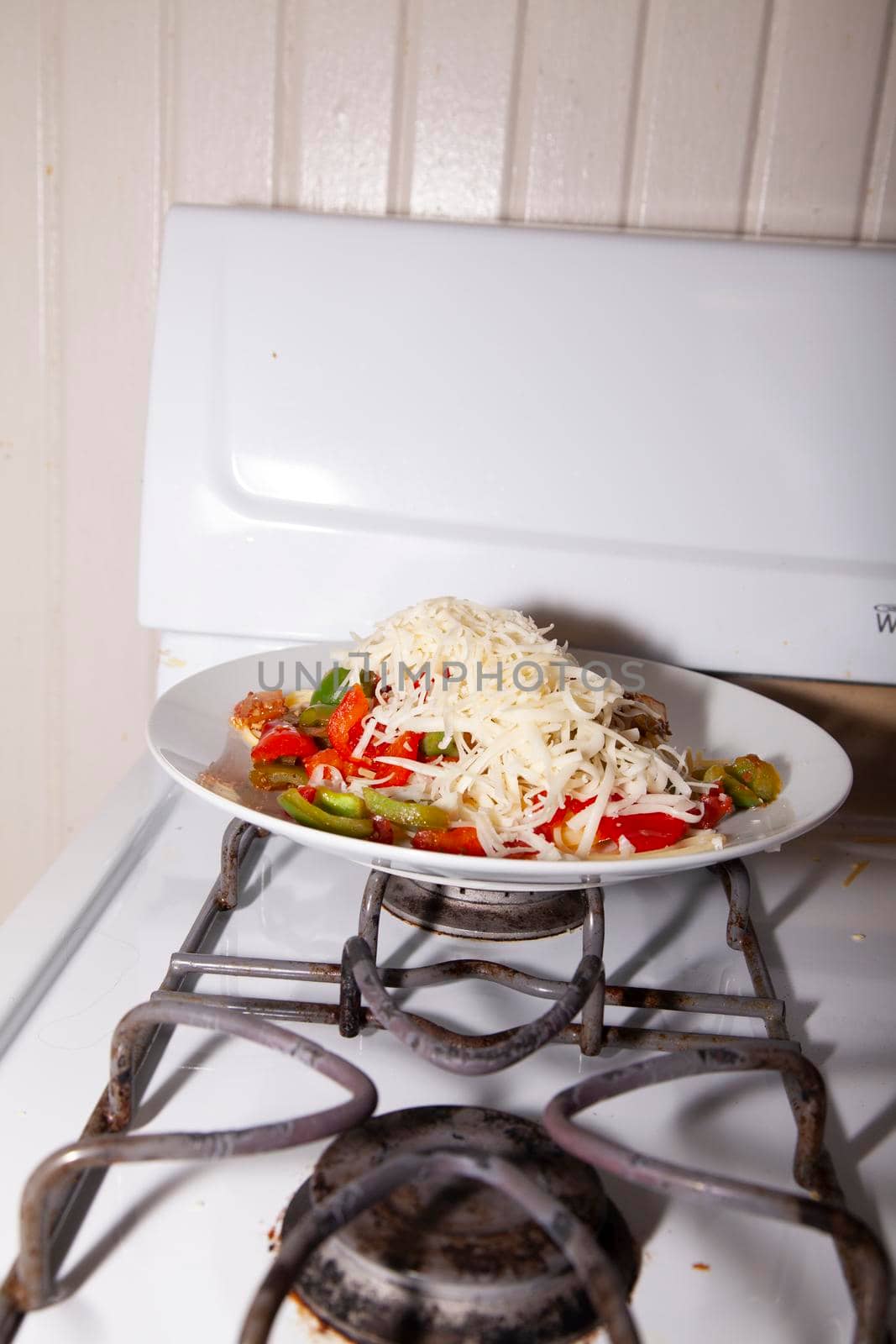 Shredded mozzarella cheese on a plate of spaghetti and bell peppers