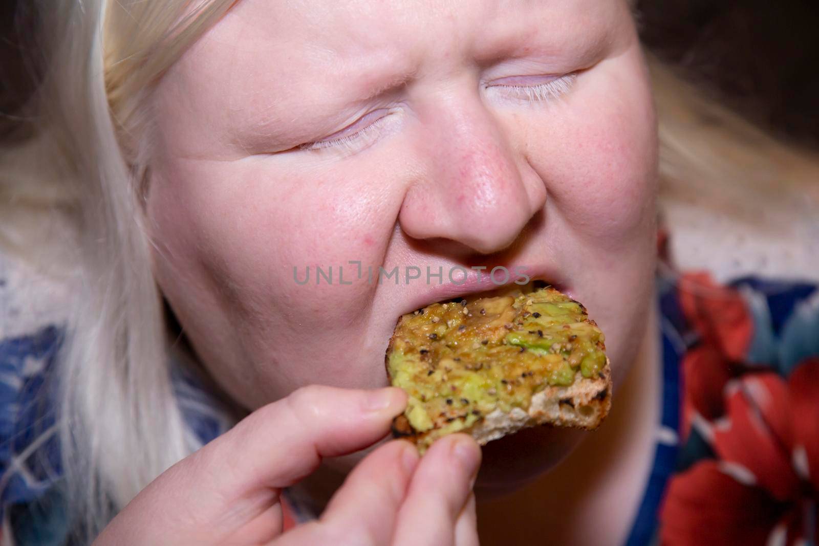 Woman eating a slice of avocado toast with her eyes closed