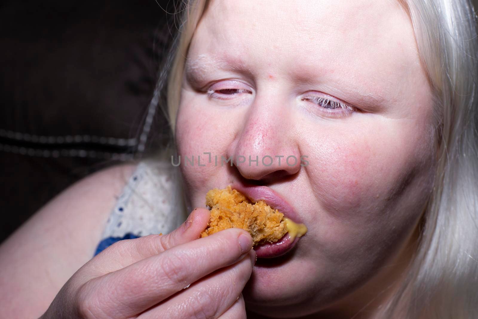 Obese, albino woman eating a chicken tender happily