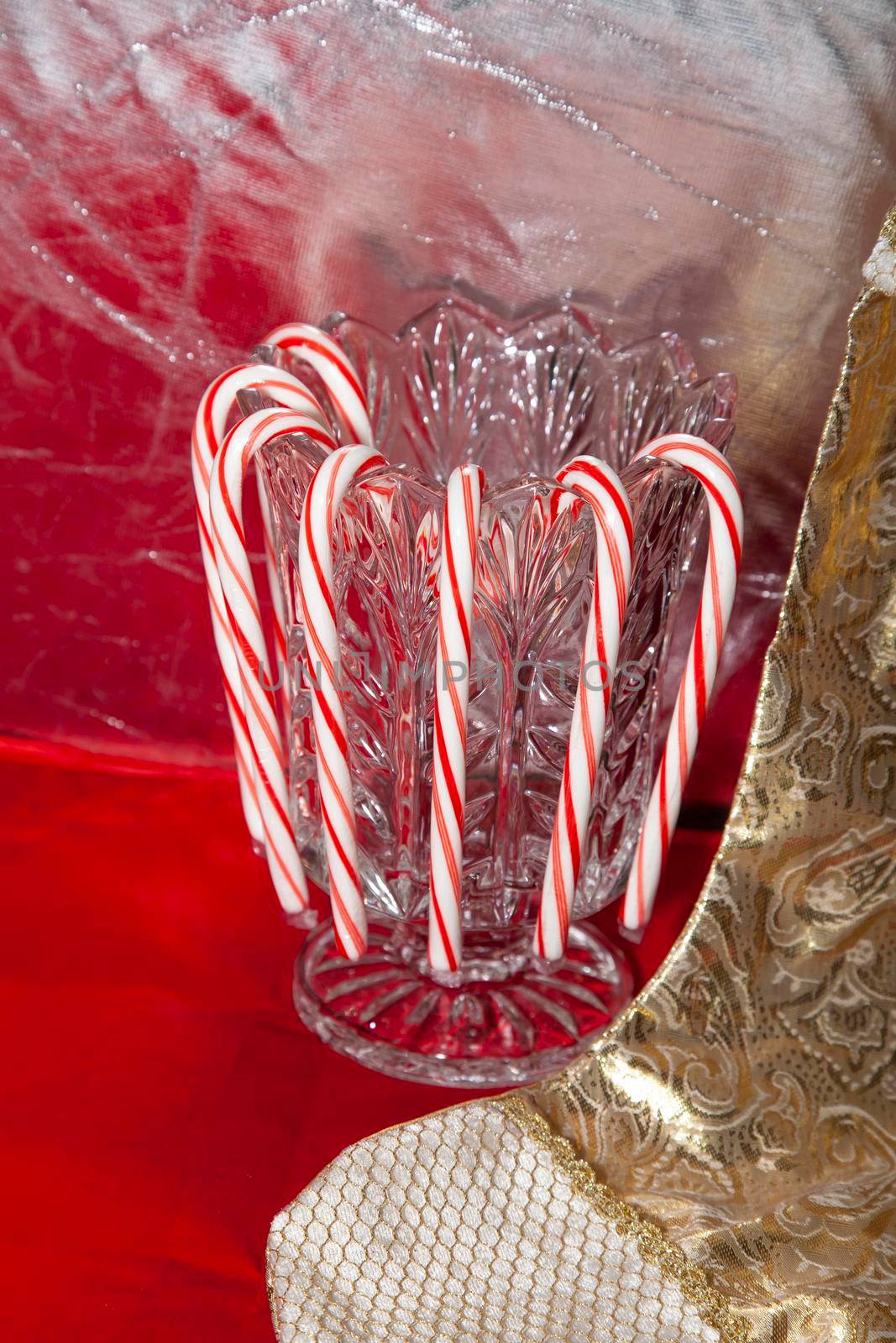 Candy canes hanging on a crystal vase next to a golden stocking