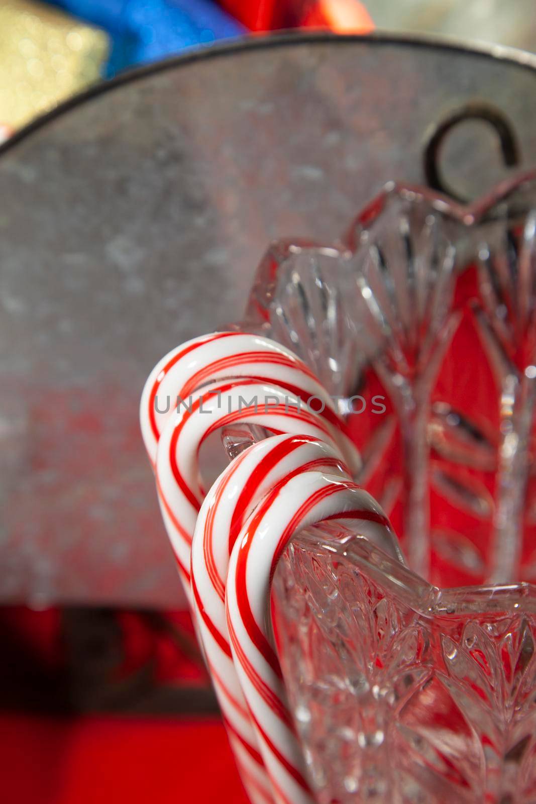 Candy canes hanging on a crystal vase next to a tin sleigh