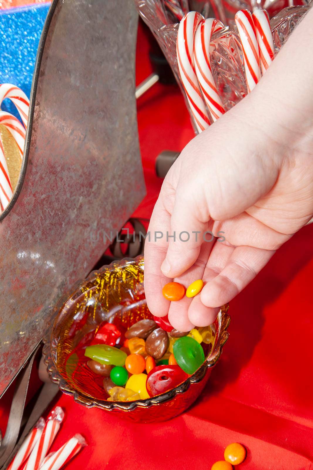 Woman grabbing multicolored candies from a bowl on a red tabletop next to a tin sleigh