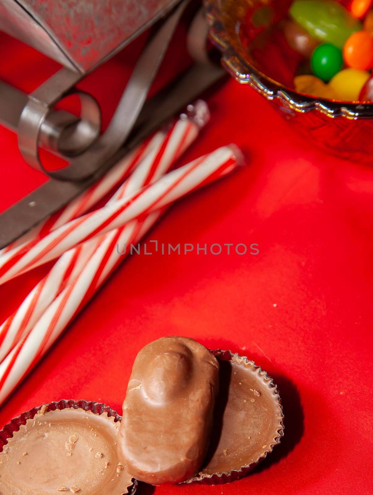 Candy canes and multicolored candies in a bowl on a red tabletop with a sleigh in the background