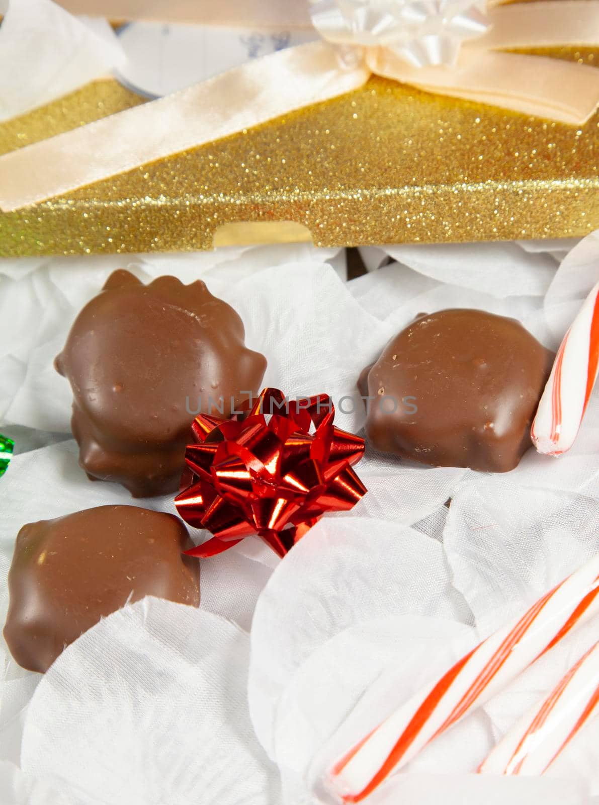 Three caramel and pecan chocolates on white petals with green and red bows, candy canes, and a gold gift package