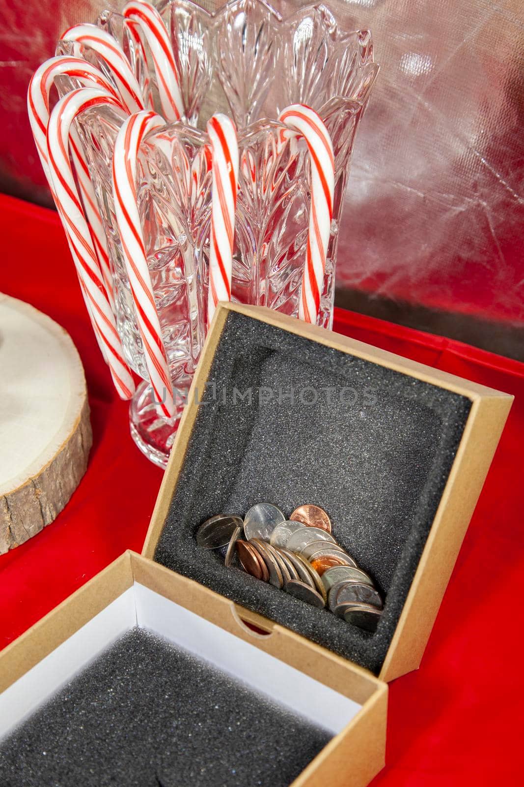 Empty, unwrapped gift box filled with pennies, nickels, dimes, quarters, and a dollar coin, on a red table top with candy canes in the background