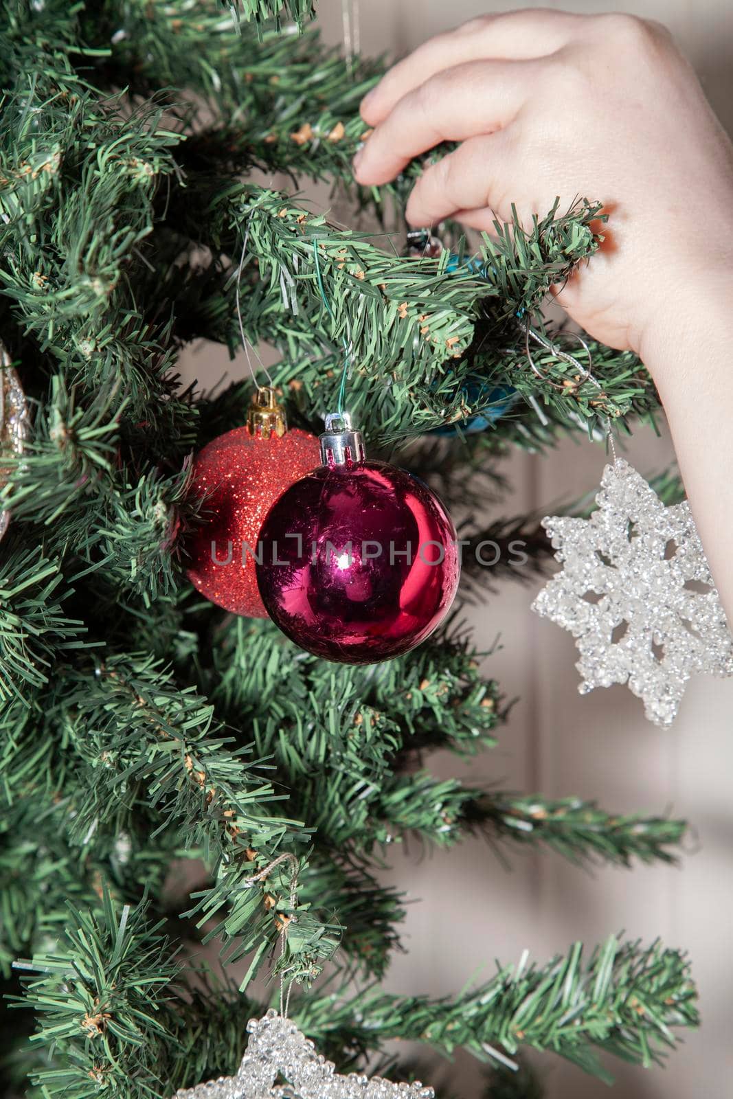 Woman hanging a blue globe on an artificial Christmas tree near purple and glittery red globes and a clear star decorations