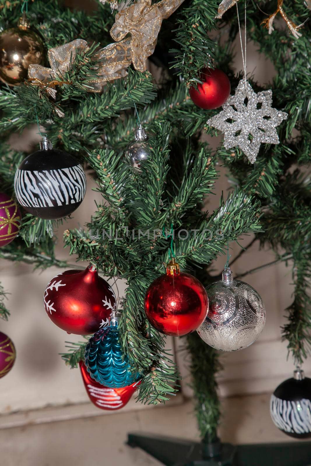 Black, silver, red, purple, and blue globe ornaments next to a red dove, a clear star ornament, and gold and white ribbon on an artificial Christmas tree