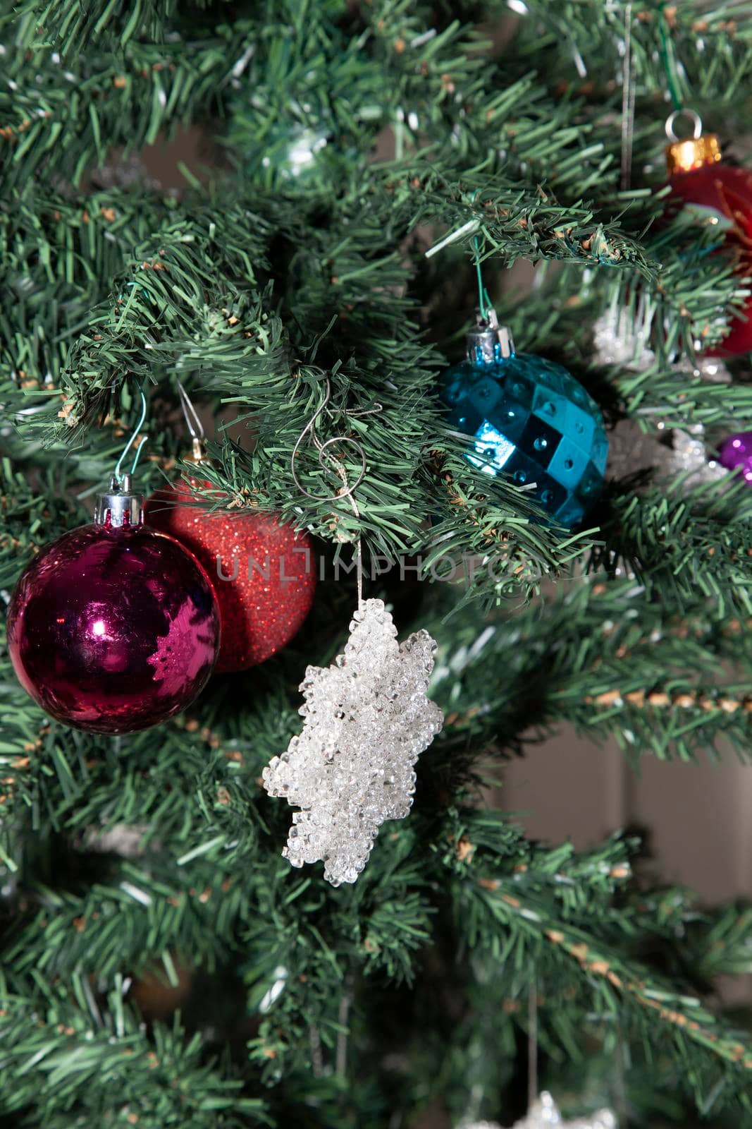 Purple, glittery red, and blue globes near a clear star decoration on an artificial Christmas tree