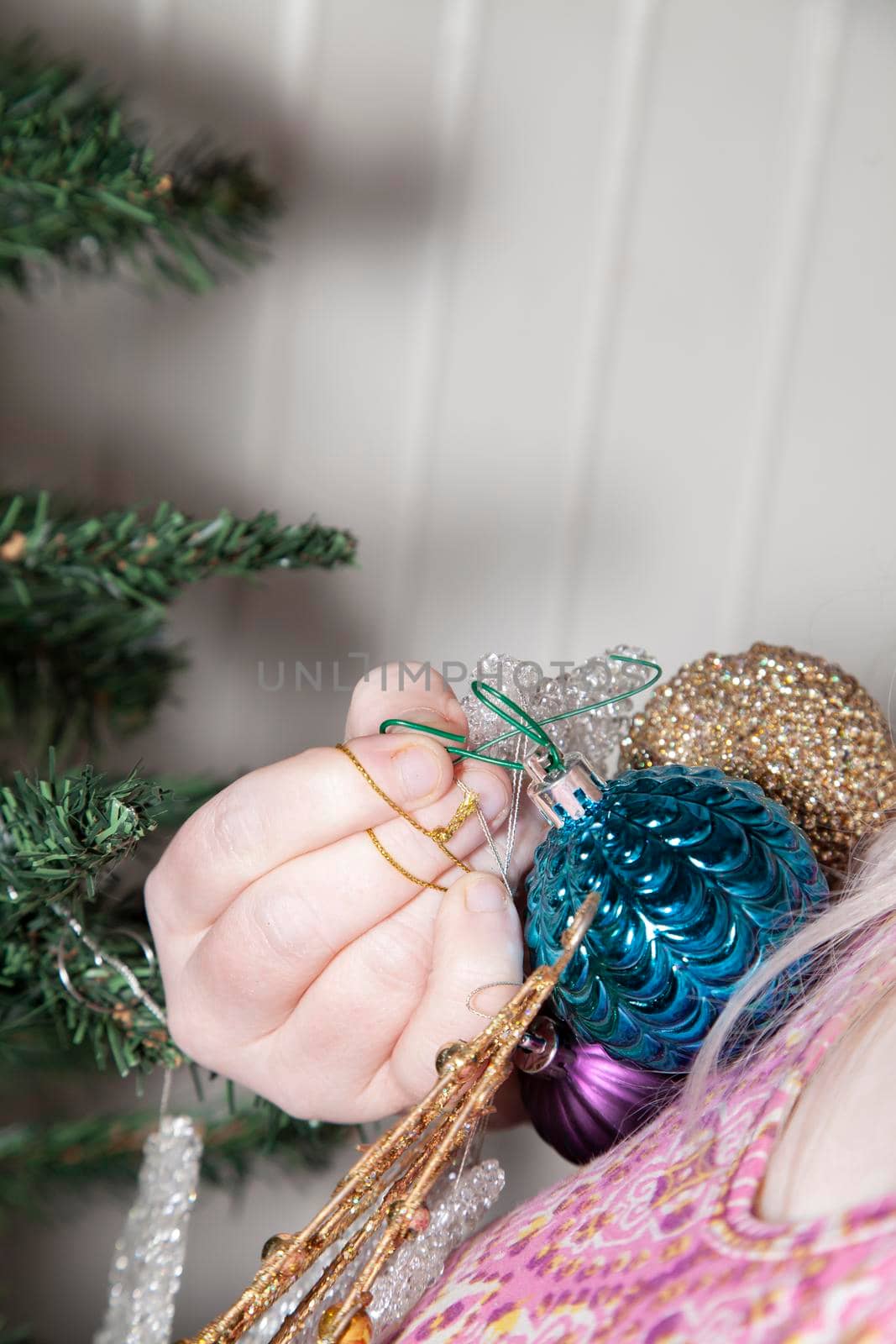 Woman holding gold, blue, and clear holiday ornaments, preparing to hang them on an artificial green Christmas tree