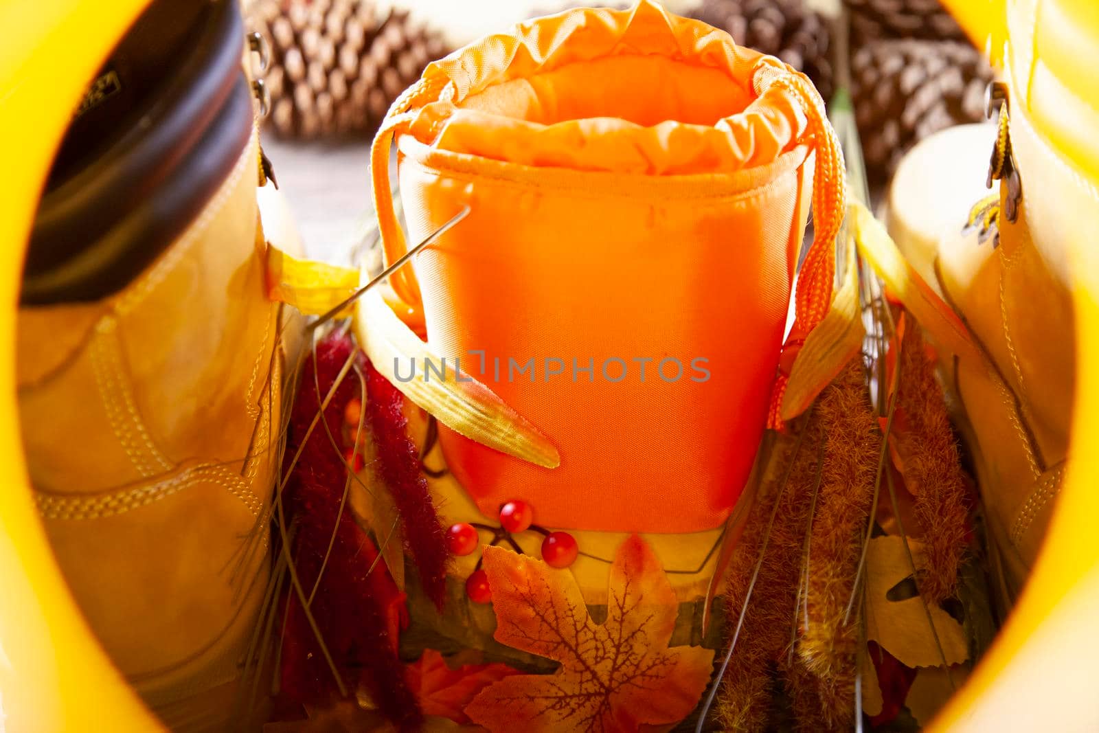 A hunter orange pouch on a wooden slab next to orange and red berries and leaves between boots with pinecones in the background