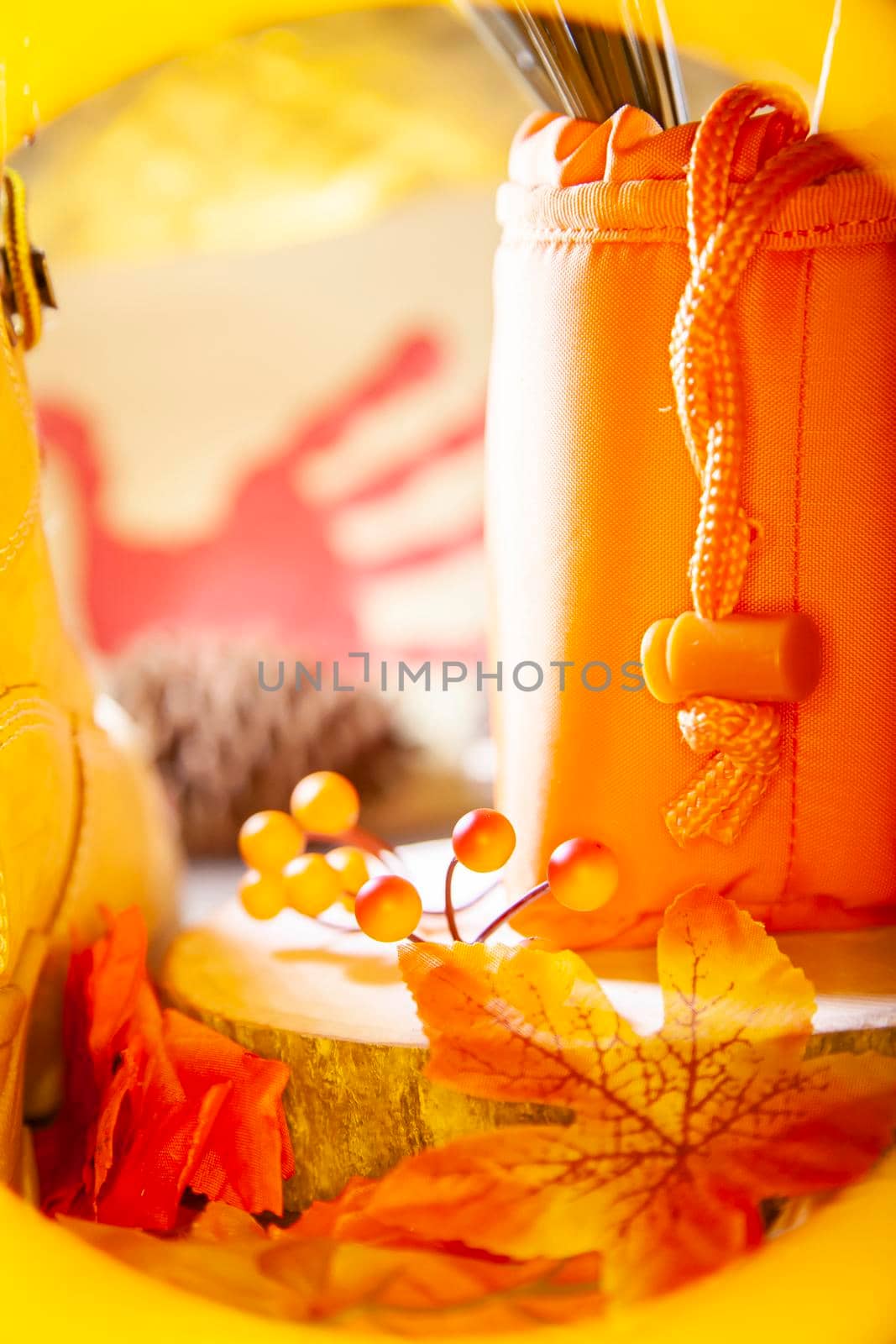 Hunter orange pouch on a wooden slab next to orange and red berries and leaves and a boot with a pinecone and a red hand turkey in the background