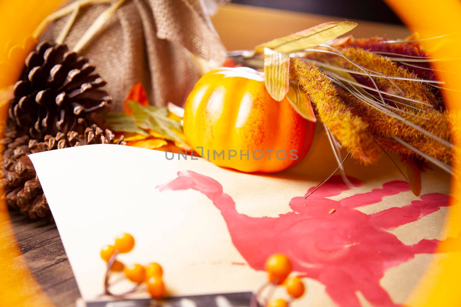 Red hand turkey on vanilla construction paper, framed in orange, with orange berries, pinecones, a small orange pumpkin, and brown foliage