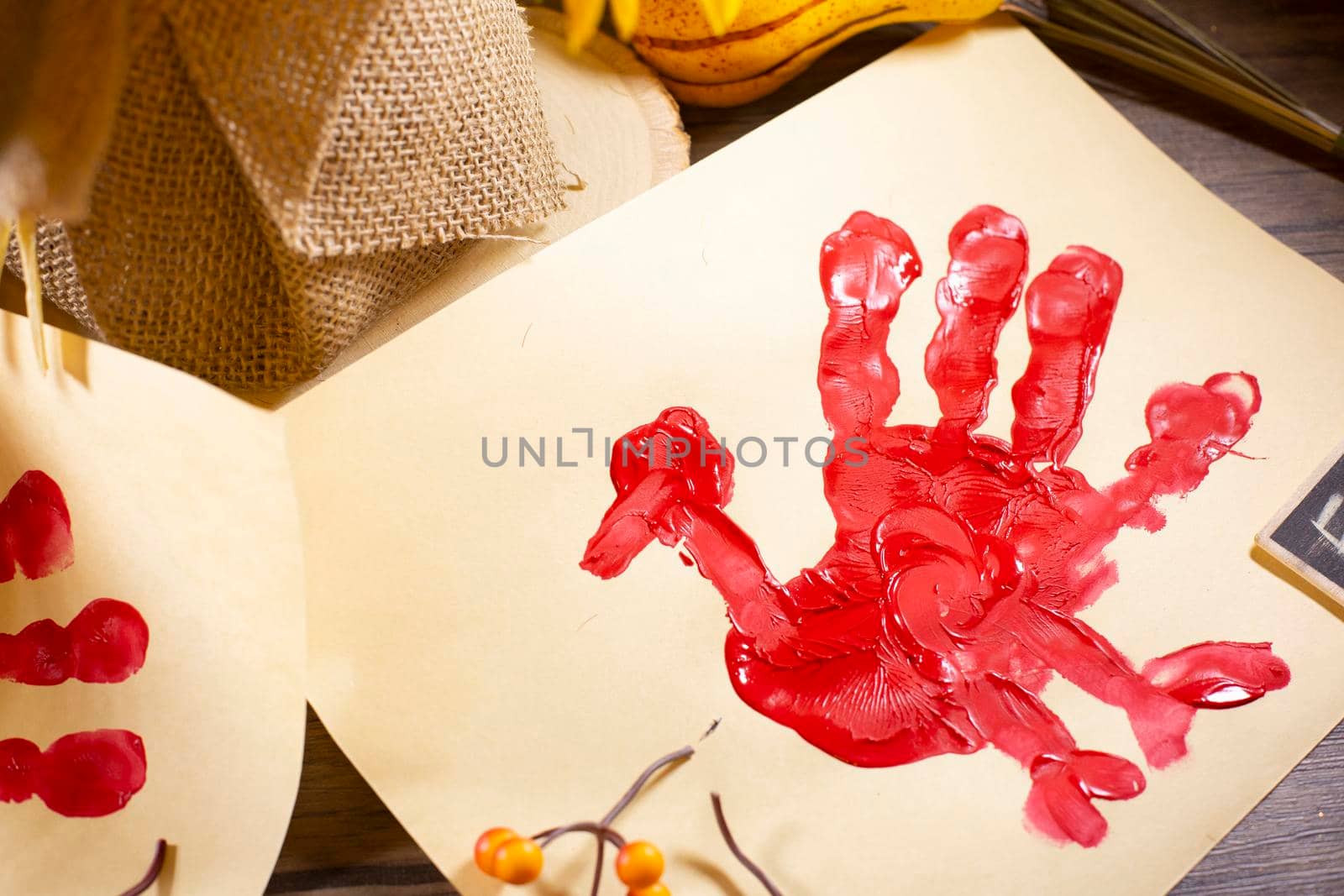 Red hand turkey on vanilla construction paper with orange berries and fall foliage on it and burlap in the background