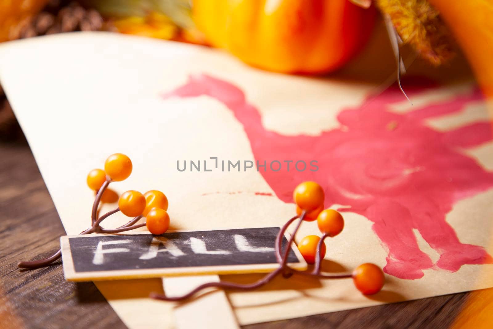 Red hand turkey on vanilla construction paper with orange berries, pinecones, a small orange pumpkin, and brown foliage with a sign that says "FALL" next to it