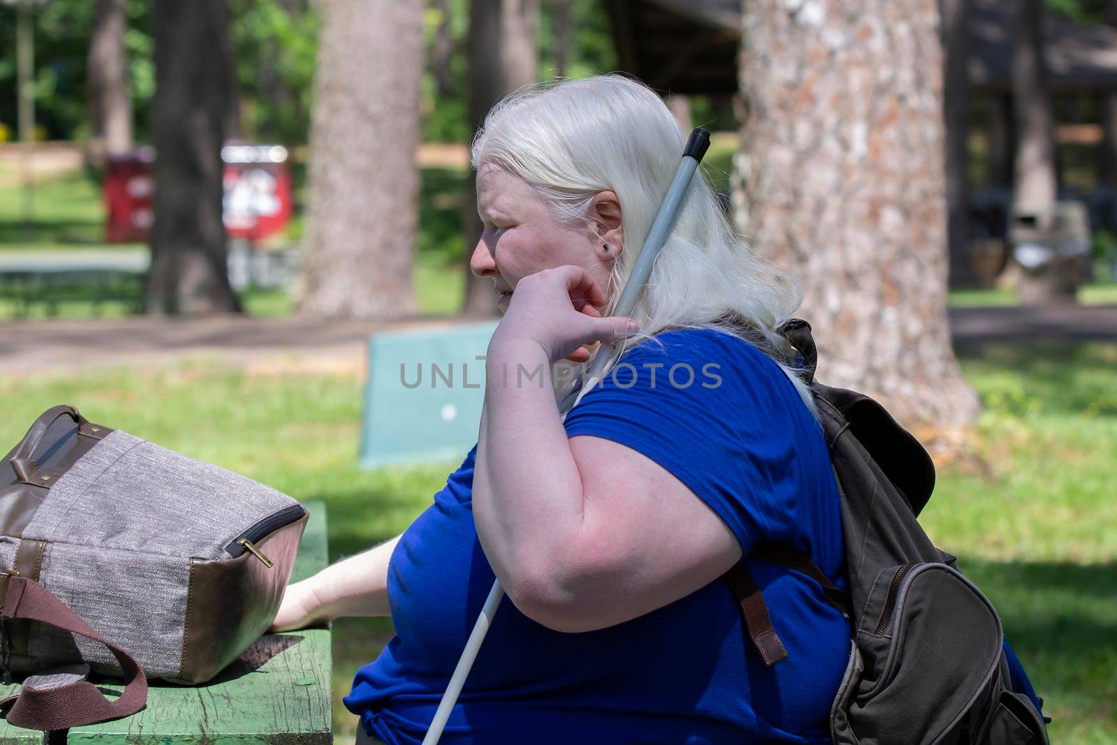 Albino woman relaxing on a park bench, with a backpack on her shoulders and an open carrying case on the table