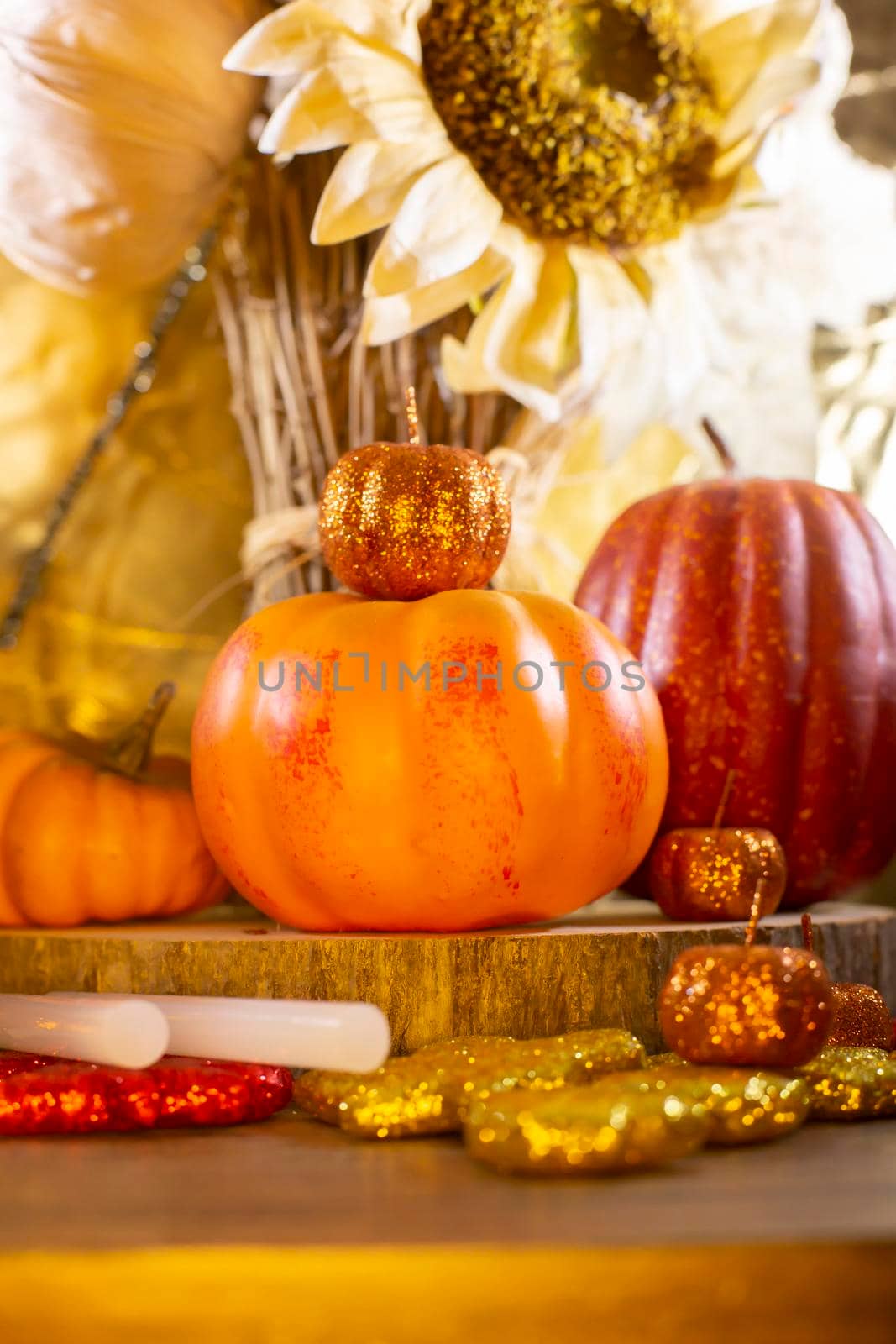 Small orange pumpkins, small red pumpkin, small orange glitter pumpkins, red, yellow, and orange glitter leaves, glue sticks for crafting, and dried sunflowers against a golden background