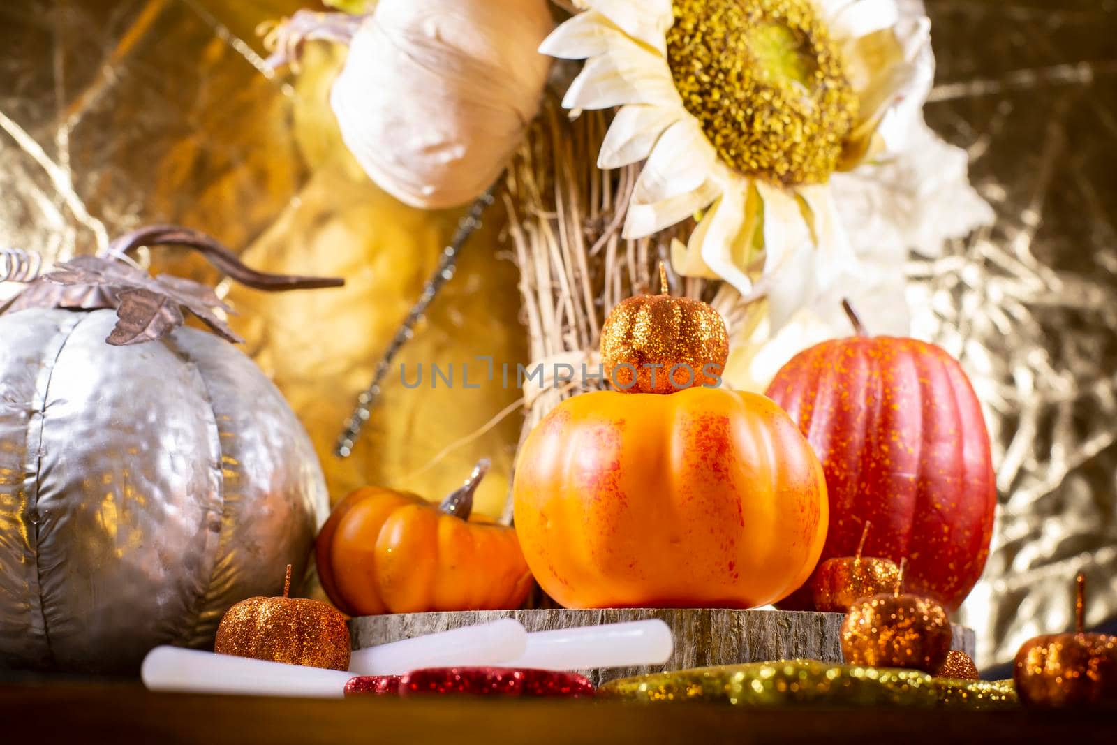 Small orange pumpkins, small red pumpkin, small orange glitter pumpkins, a large silver pumpkin, red, yellow, and orange glitter leaves, and dried sunflowers against a golden background