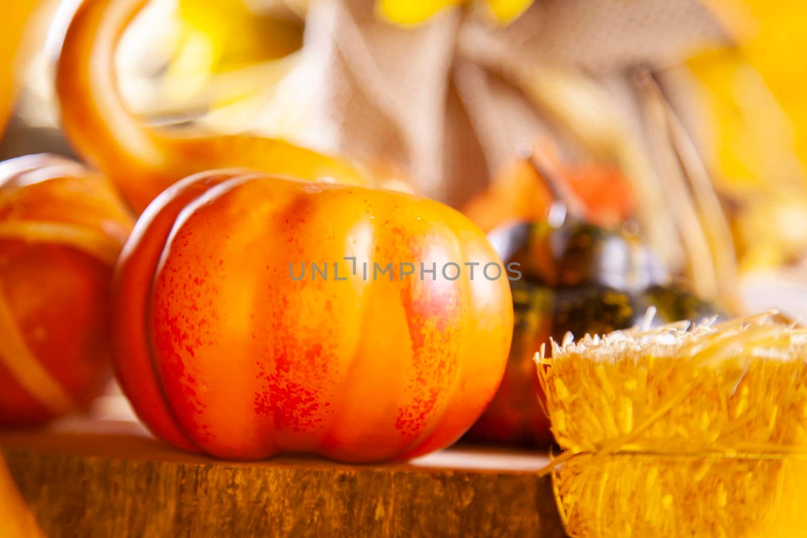 Small orange pumpkin on a wooden platform next to a small bale of hay, with a golden tone