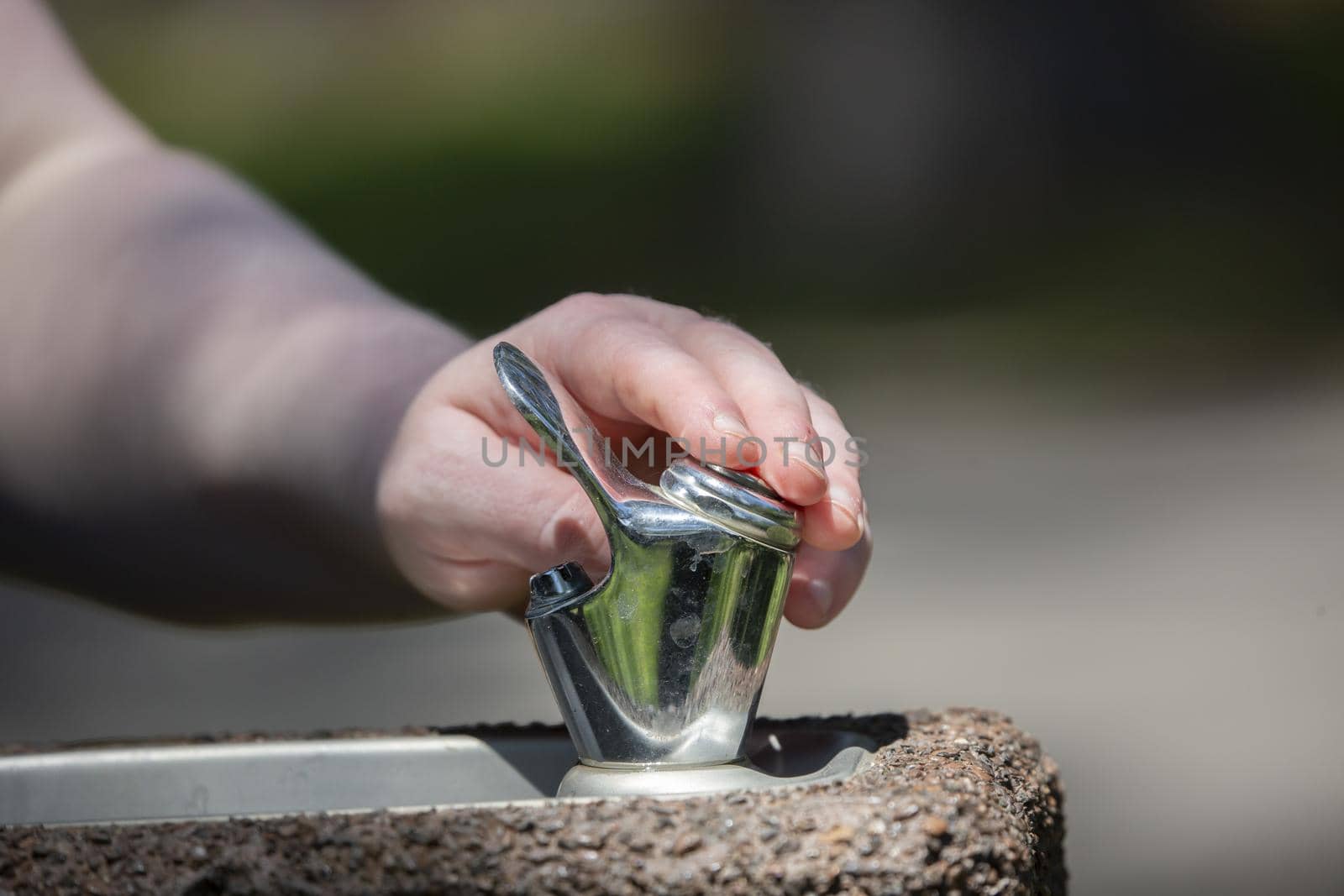 Woman pushing the button to drink from outdoor water fountain