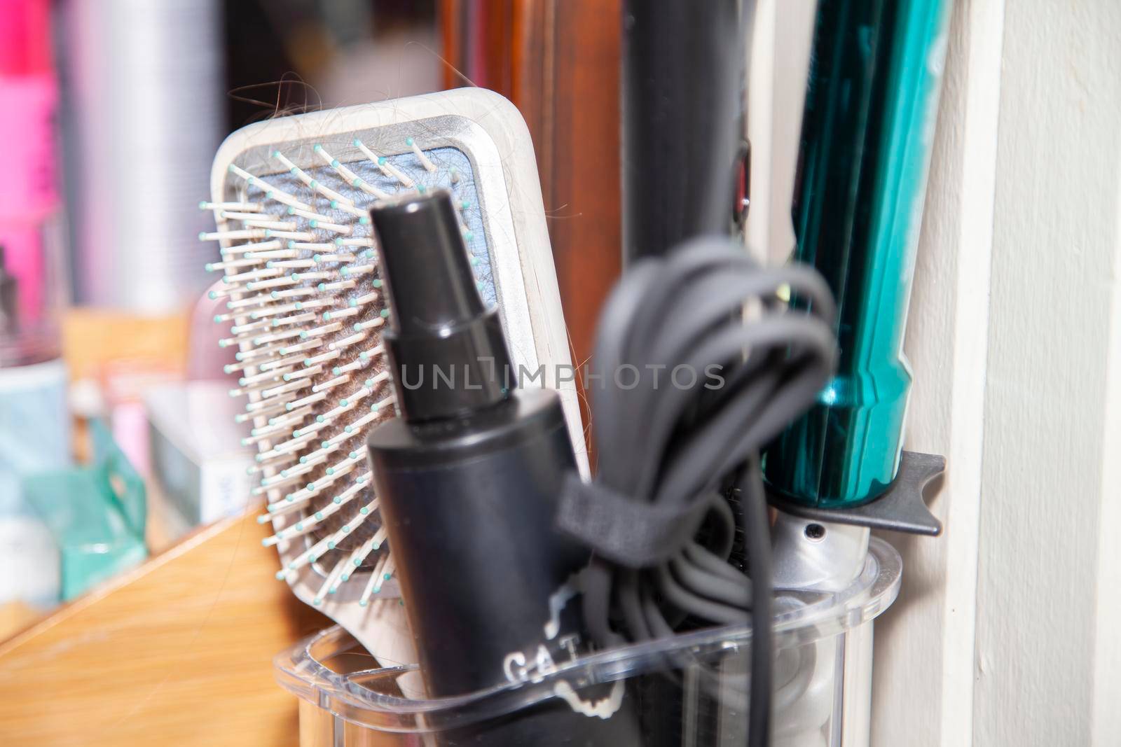 Hair brush with hair in it, spray, and styling tools with a mirror and makeup in the background