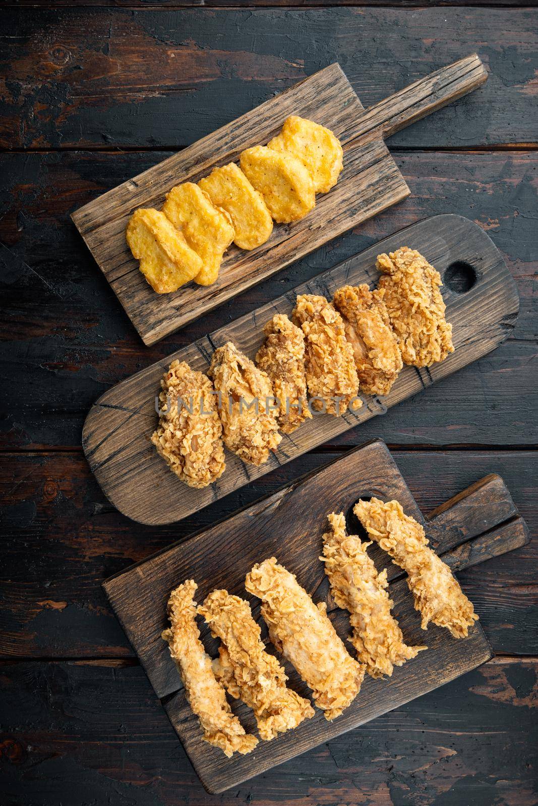 Breaded fried chicken parts on dark wooden background, top view.