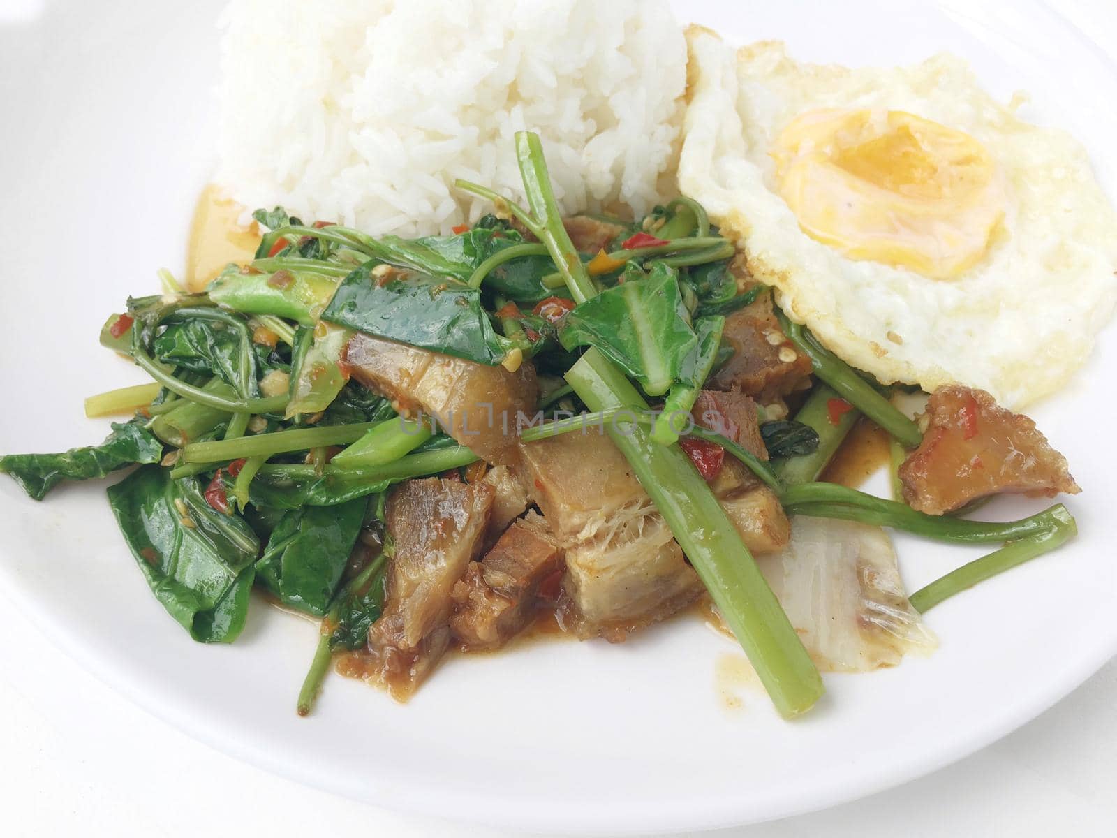 Stir-fried Crispy Pork with Kale and thai style fried egg in white plate on white background. Thai style fast food make by order.