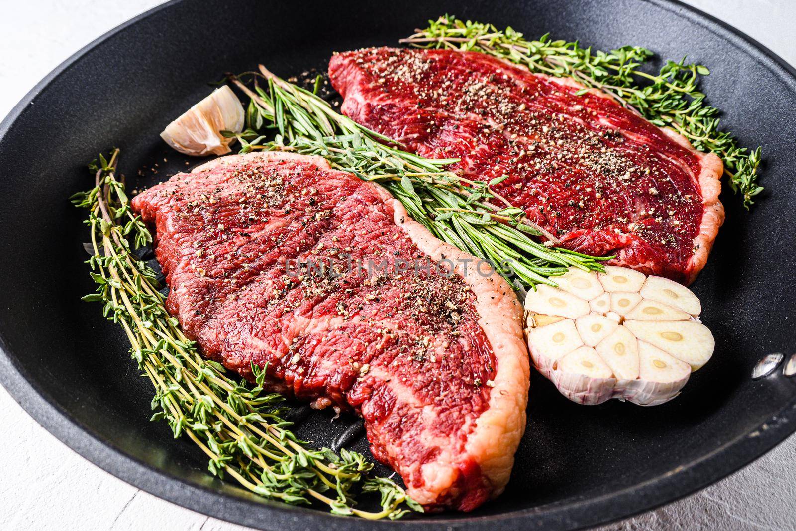 Two raw picanha organic beef steaks ready for grill on pan with herbs and garlic. Over white textured background, side view selective focus, new wide angle